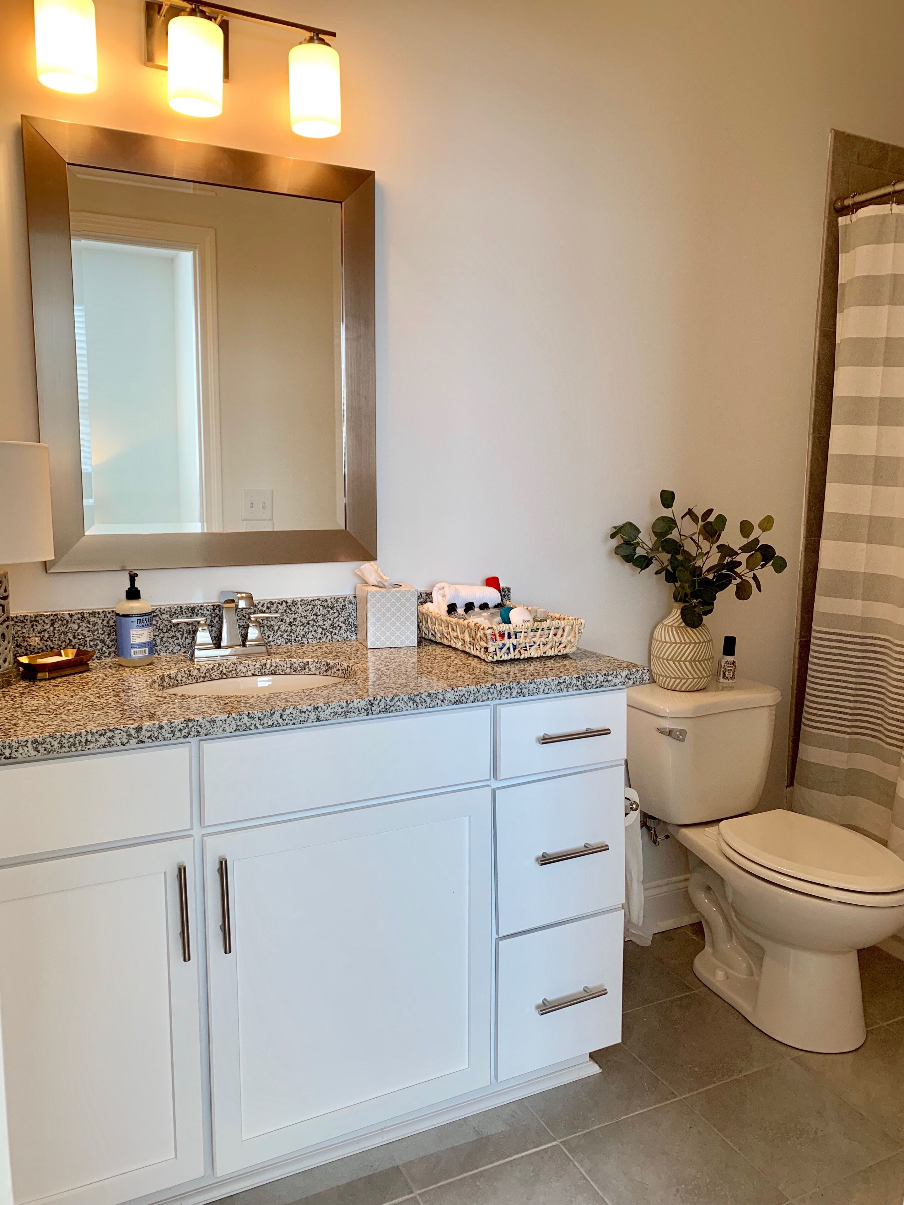 A bathroom with a granite countertop, white cabinets, a large mirror, and a toilet.