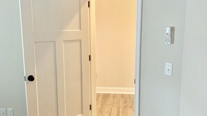 A room with a wooden floor, a white door, and an air conditioning unit mounted on the wall. - 1-Bedroom Condo Just 1 Block from the Beach and Steps from the Hampton Strip (Hampton)
