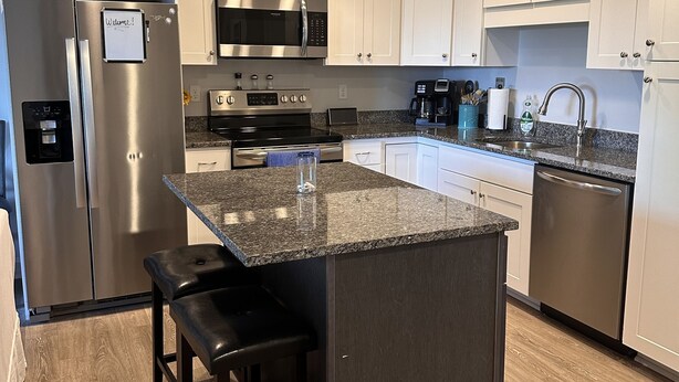 A modern kitchen with stainless steel appliances, a granite countertop island, and white cabinetry. - 1-Bedroom Condo Just 1 Block from the Beach and Steps from the Hampton Strip (Hampton)