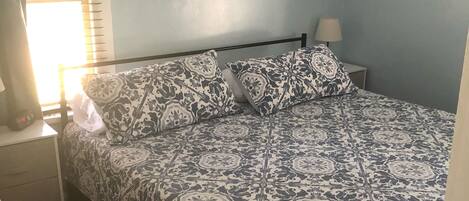 A bedroom with a bed, a nightstand, a lamp, a painting, and a poster on the wall.