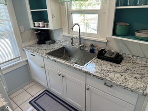 A kitchen with a stainless steel sink, granite countertop, white cabinets, and a window with a view of the outside.