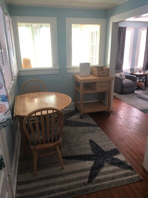 Uma sala de jantar com mesa e cadeiras de madeira, uma pequena mesa lateral de madeira e um tapete com padrão de estrelas sobre um piso de madeira.