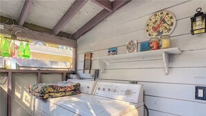 Een wasruimte met een wasmachine, een plank met decoratieve spullen en een wandklok.