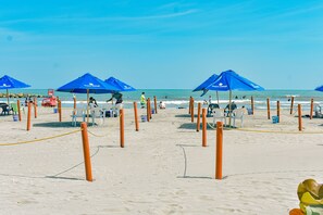A beach with blue umbrellas, wooden posts, and beach chairs. - Hotel Isla Capri (Cartagena)