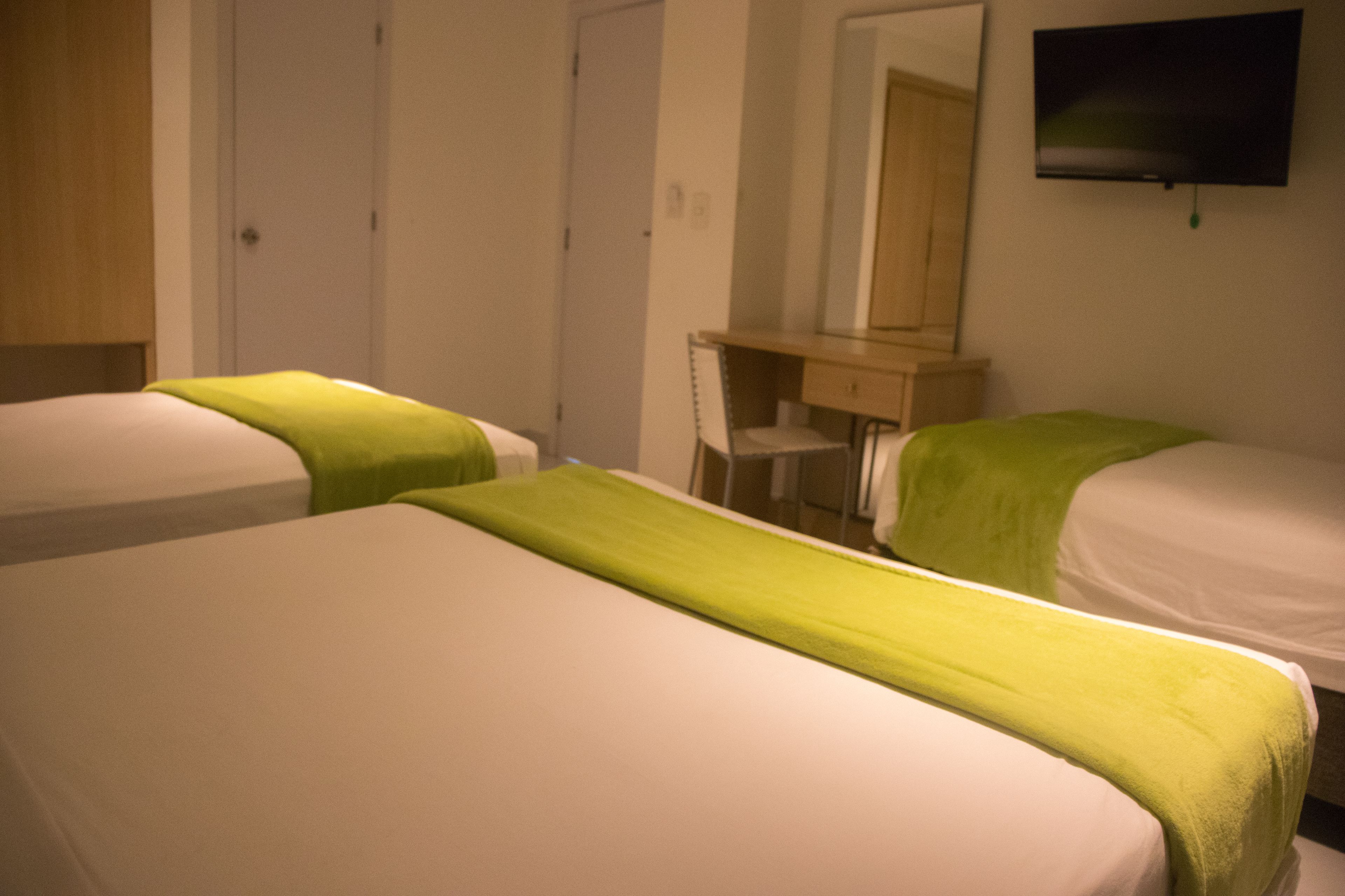 A hotel room with two beds, a wooden wardrobe, a mirror, and a television on the wall.