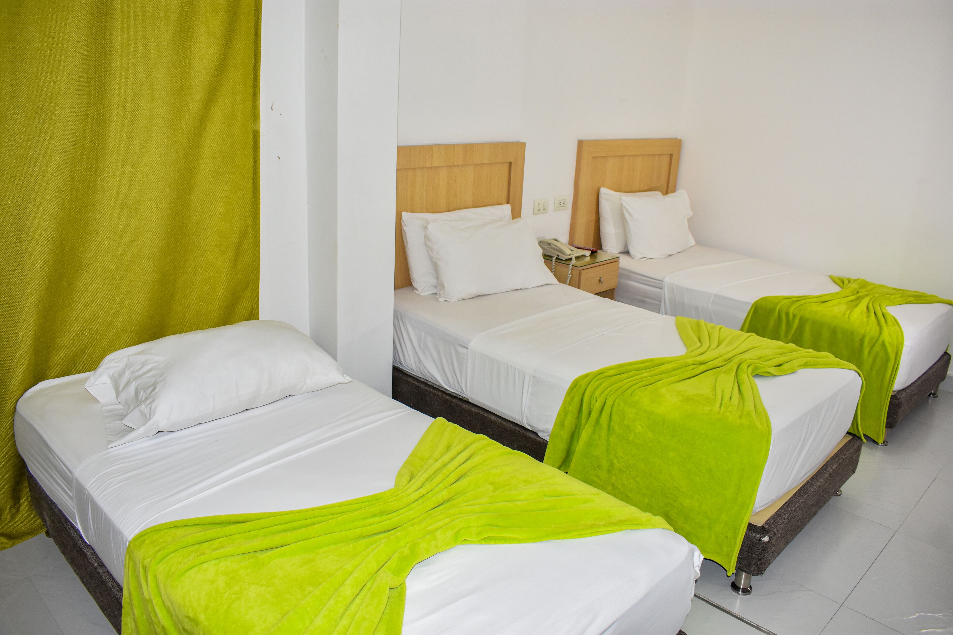A hotel room with three single beds, each with a wooden headboard and white bedding.