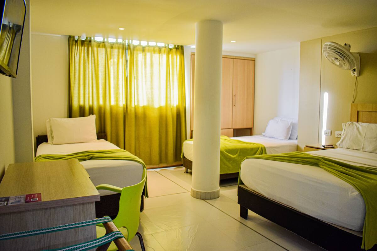 A hotel room with two beds, a desk, a chair, a fan, and a window with curtains.
