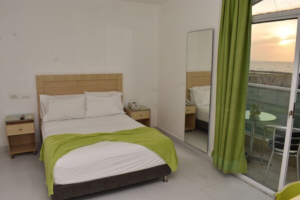 Una habitación de hotel con cama, mesitas de noche, un espejo y vista a la playa a través de un ventanal corredero.