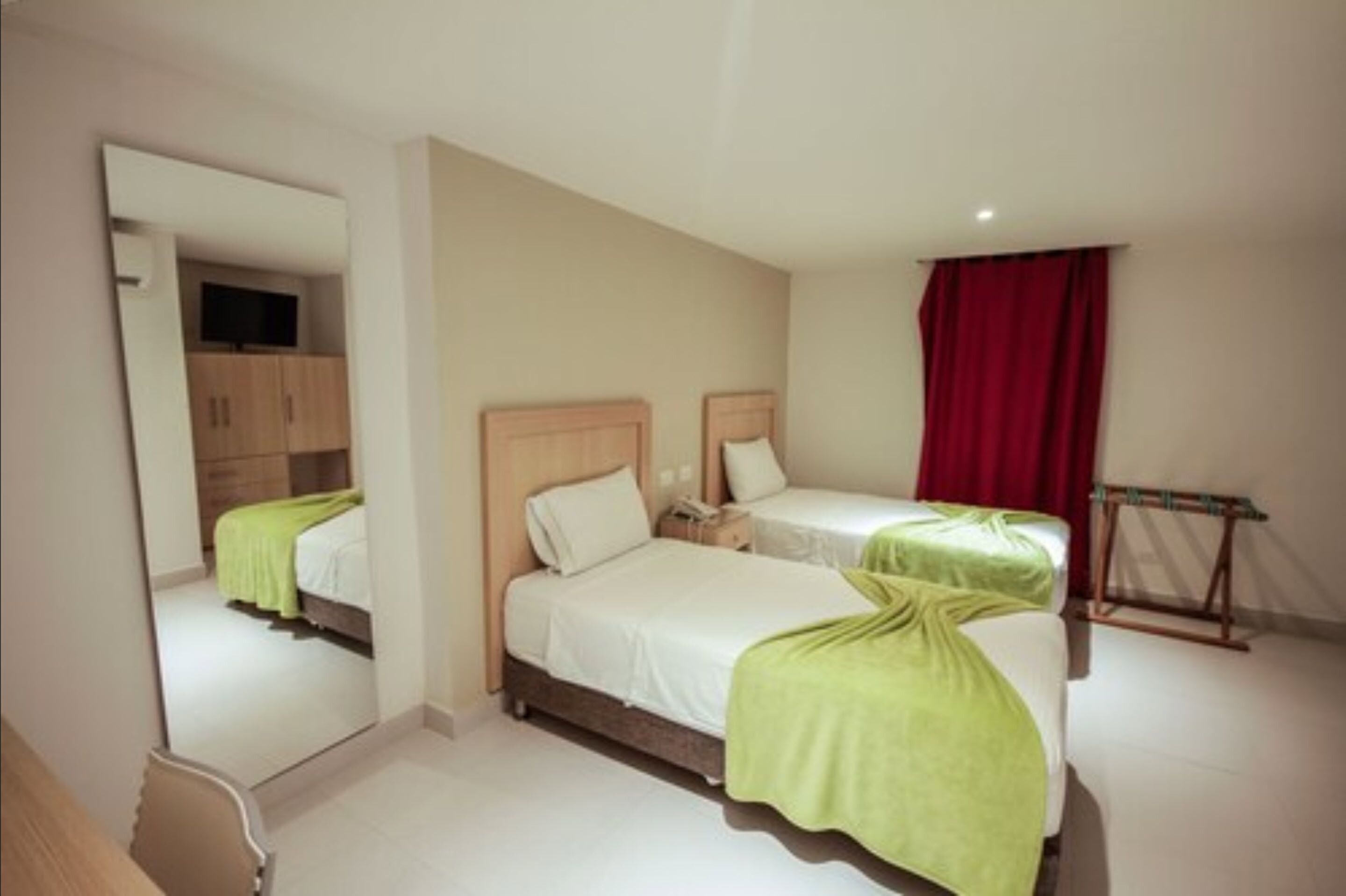 Une chambre d’hôtel avec deux lits, un miroir, une armoire et un rideau rouge.