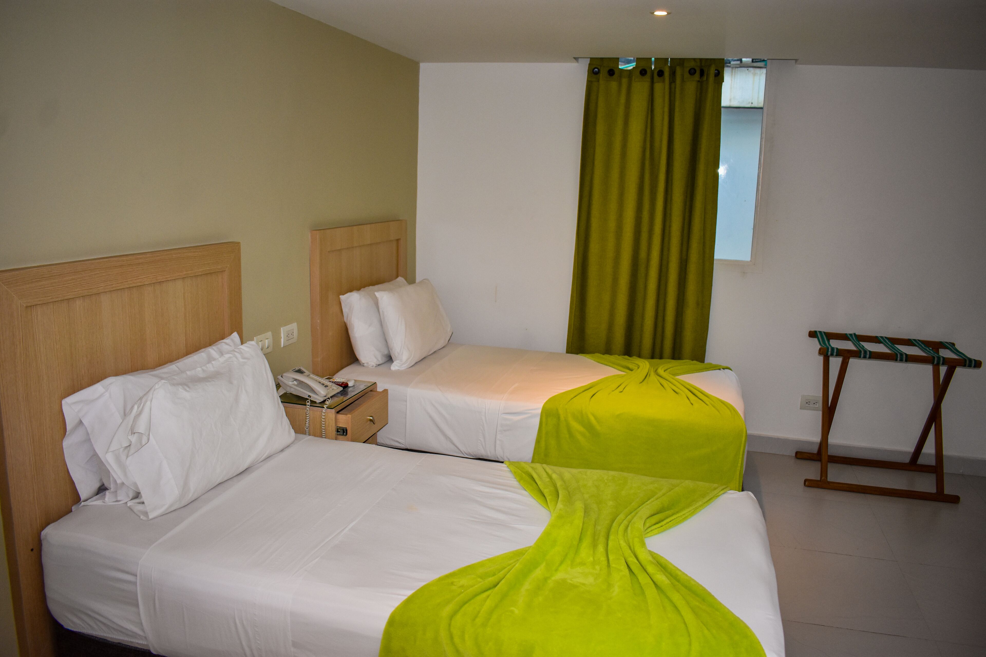 A hotel room with two beds, a small table, and a window with curtains.