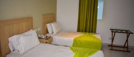 A hotel room with two beds, a small table, and a window with curtains.