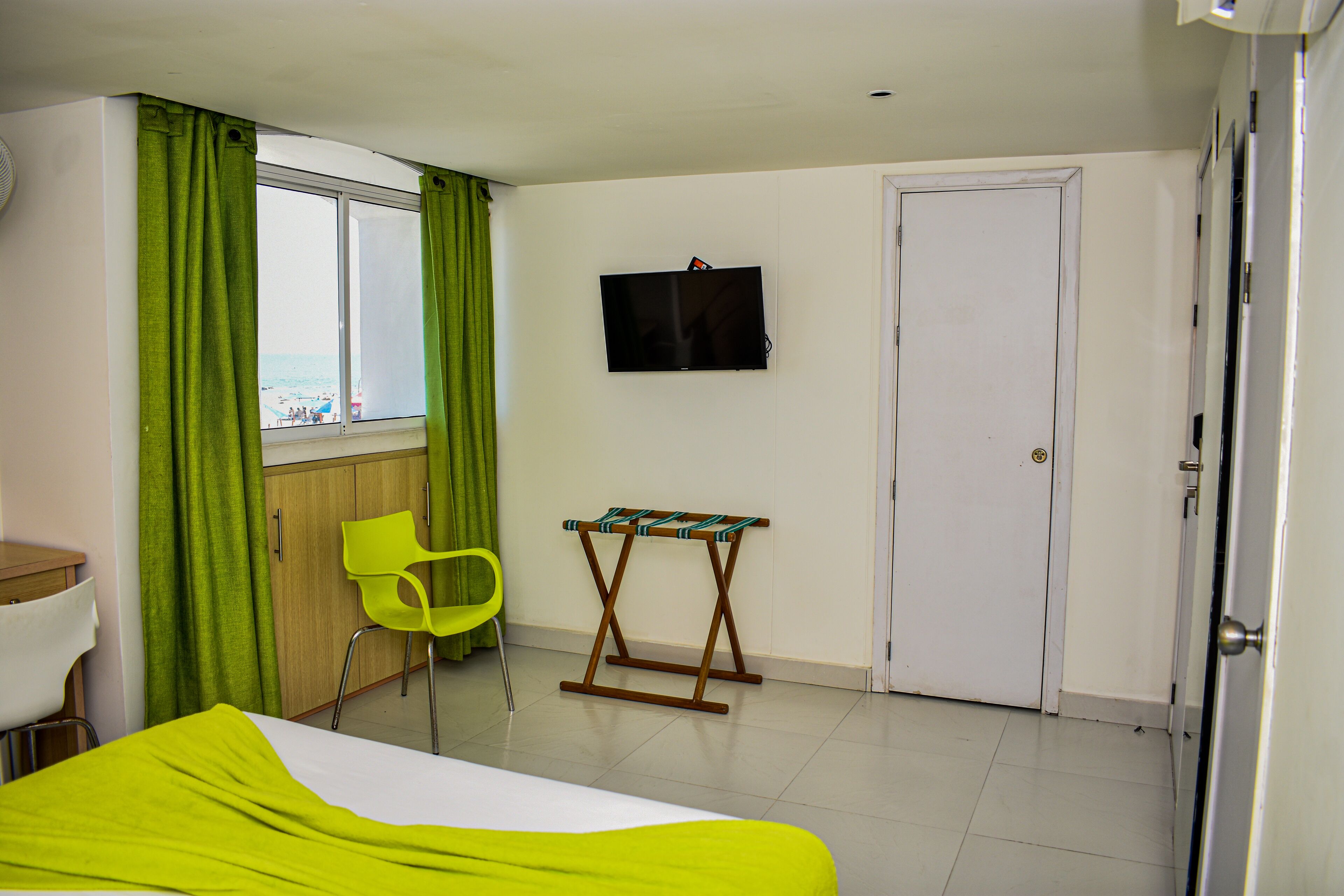 Une chambre d’hôtel comprenant un lit, un téléviseur fixé au mur, une fenêtre avec des rideaux, une armoire en bois et une chaise.