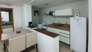 A compact kitchen with a dining area, white appliances, and a small island. - Rosa Branca apartments (Ponta Verde)