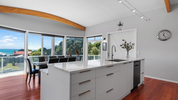 A modern kitchen with a large island, white cabinetry, and a view of the sea. - Sea Shells By The Shaw  - Waihi Beach Holiday Home (Waihi Beach)