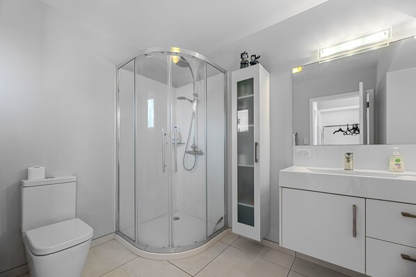 Un bagno moderno con doccia vetrata, un water, un lavabo con specchio e un armadietto.