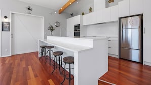 A modern kitchen with white cabinetry, a stainless steel refrigerator, and a wooden floor. - Sea Shells By The Shaw  - Waihi Beach Holiday Home (Waihi Beach)