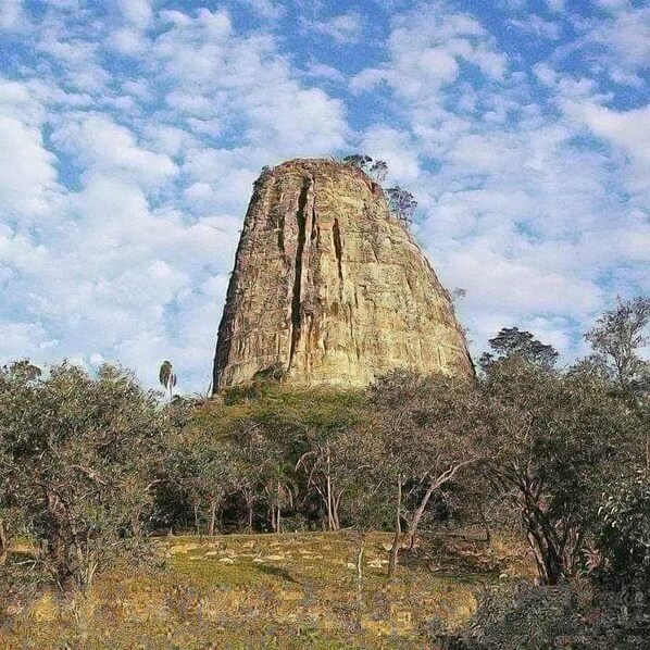 A large, isolated rock formation surrounded by sparse vegetation.