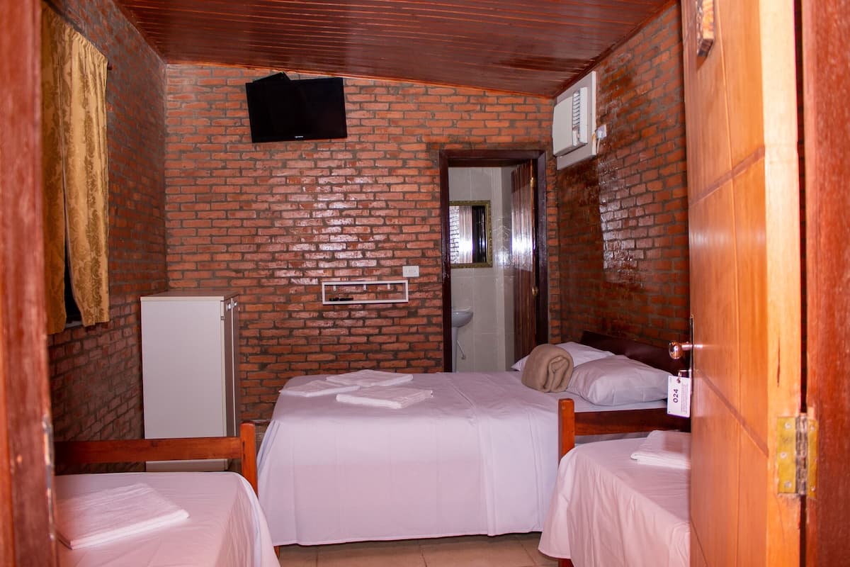 A room with two beds, a white refrigerator, a wooden door, and a brick wall.