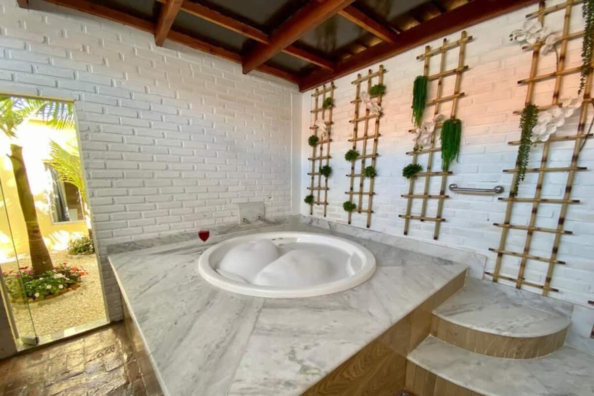 A bathroom with a marble countertop, a built-in jacuzzi, and a wooden wall with decorative plants.