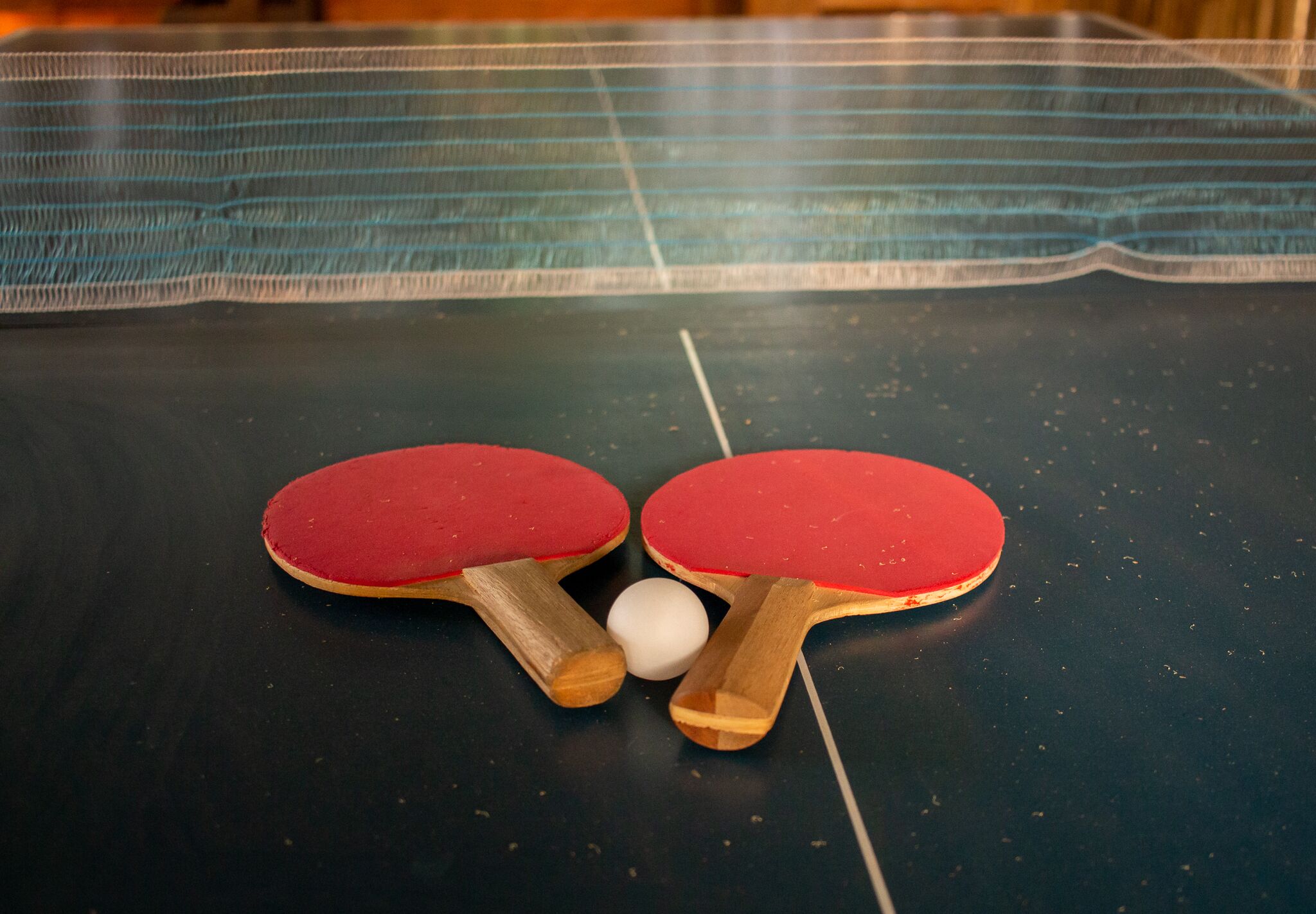Una mesa de tenis de mesa con dos paletas rojas y una pelota blanca.