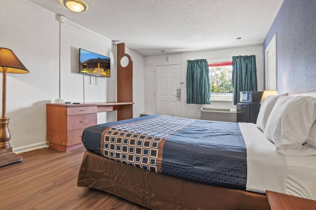Une chambre d’hôtel avec un lit, un bureau, une télévision et une fenêtre avec des rideaux.