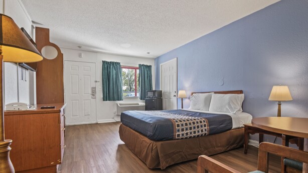 A hotel room with a bed, a desk, a chair, a lamp, a TV, and a window with curtains. - Economy Lodge (Portsmouth)