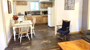 Cucina con mobili in legno, un tavolo da pranzo con sedie, un frigorifero e un quadro appeso al muro.