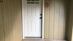 Una porta bianca con un cartello che riporta la scritta 'WELCOME Y'all', un campanello nero e il numero '3' di colore rosso sulla parete.
