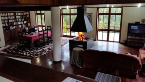 Amplia sala de estar con chimenea, comedor con mantel rosa y una gran estantería.