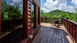 A wooden deck with a table and chairs, surrounded by a wooden railing, overlooking a forested area. - 2BR 2BTH PRIVATE, HOT TUB POOL TABLE (Sevierville)