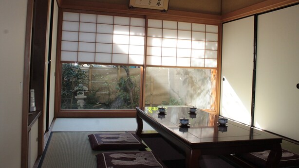 Um quarto japonês tradicional com piso de tatame, portas corrediças shoji e uma mesa baixa com jogos de chá.
