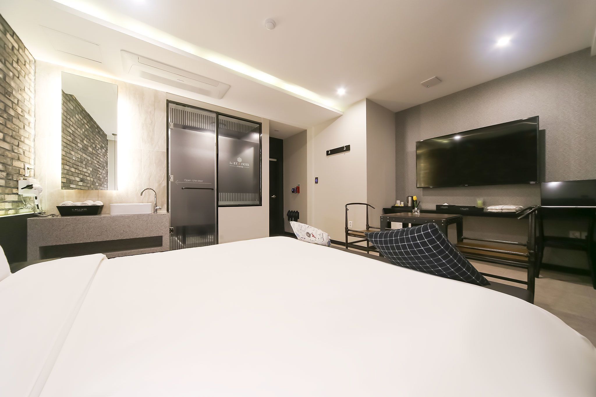 A modern hotel room with a large bed, a flat-screen TV, a desk, and a bathroom with a mirror and sink.