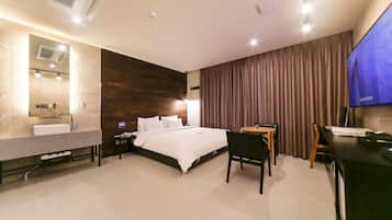 A modern hotel room with a large bed, a desk, a chair, a TV, a bathroom with a sink, and a mirror.