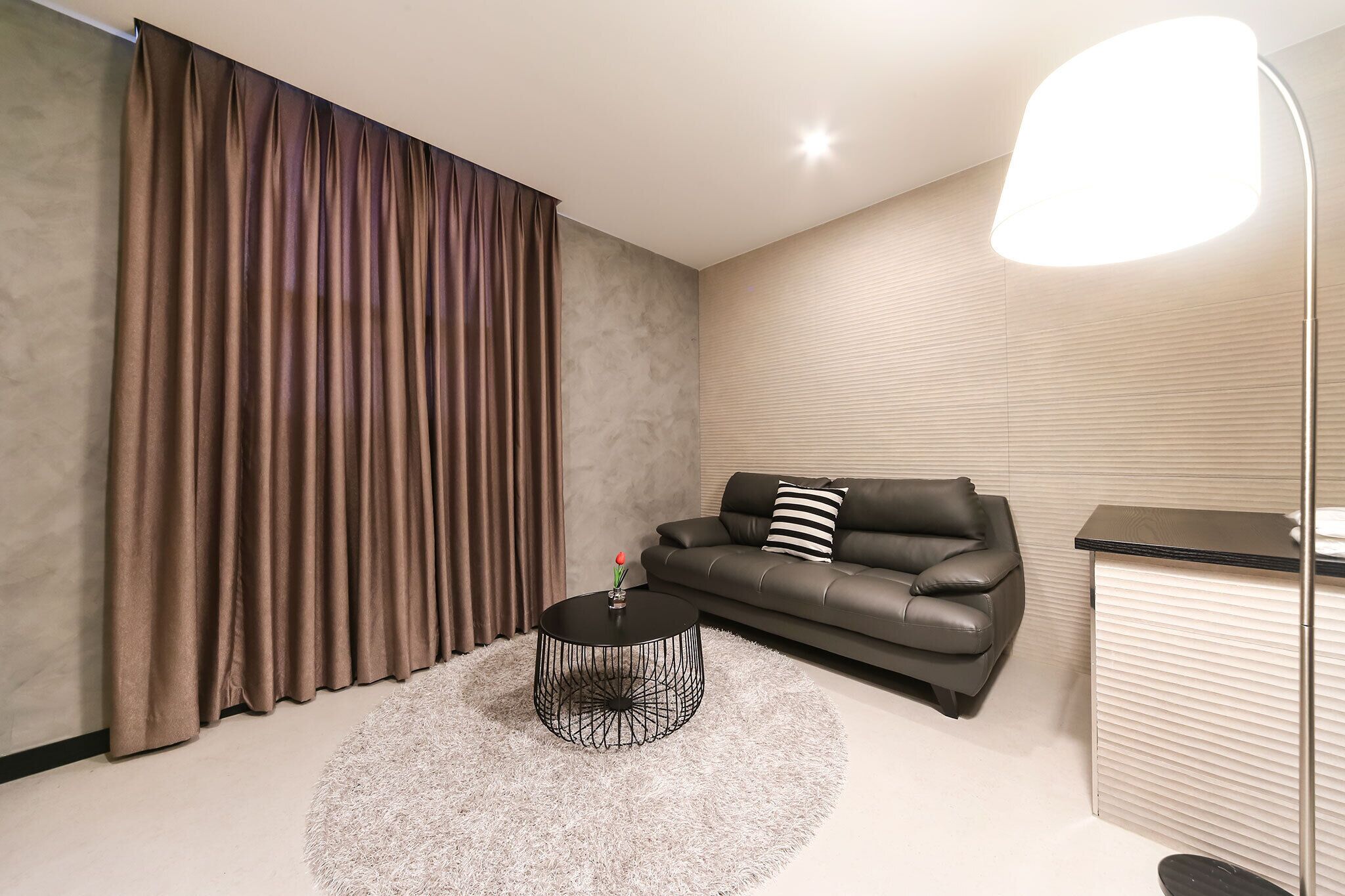 Un salon moderne avec une table basse ronde noire, un canapé en cuir noir et une grande fenêtre avec des rideaux.