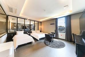 A hotel room with two beds, a desk, a chair, a round rug, and a large window with curtains. - Le Idea Hotel (Gyeongju)