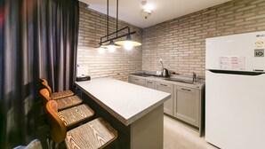 A modern kitchen with a brick backsplash, a white refrigerator, a built-in oven, and a bar area with a wooden chair and bench. - Le Idea Hotel (Gyeongju)