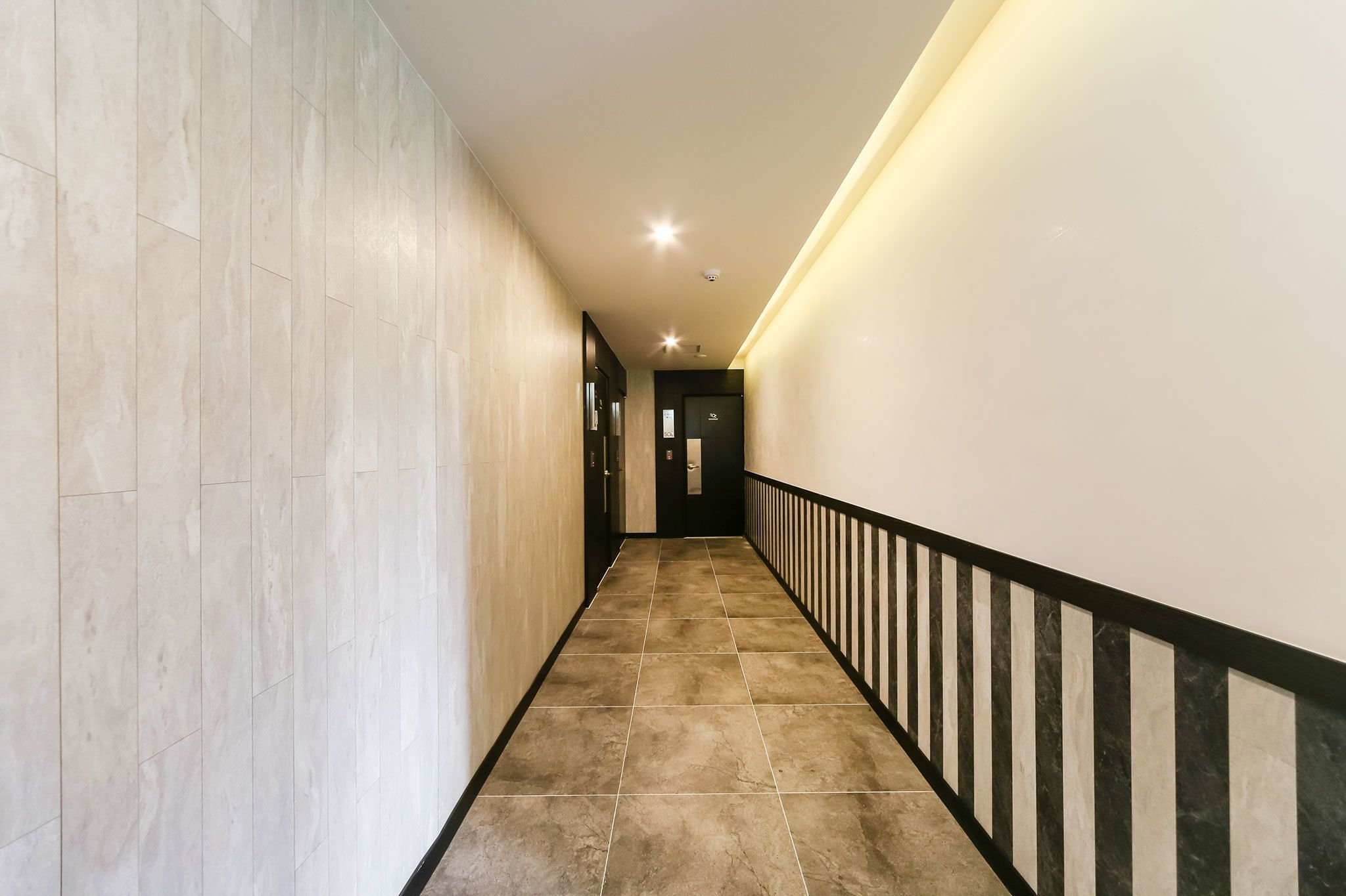 Um corredor com piso de azulejos, corrimão preto e branco e uma porta no final.
