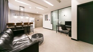 A modern hotel room with a leather sofa, a round coffee table, a dining area with a brick wall, and a separate desk area with a computer. - Le Idea Hotel (Gyeongju)