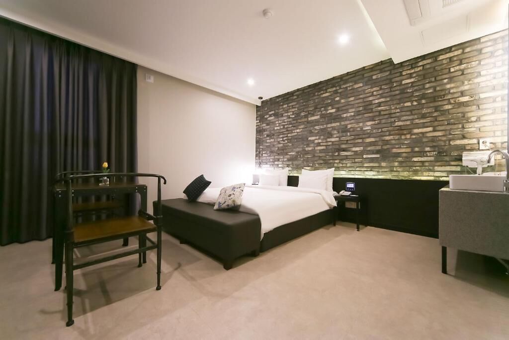 A modern hotel room with a bed, a desk, a chair, and a bathroom.