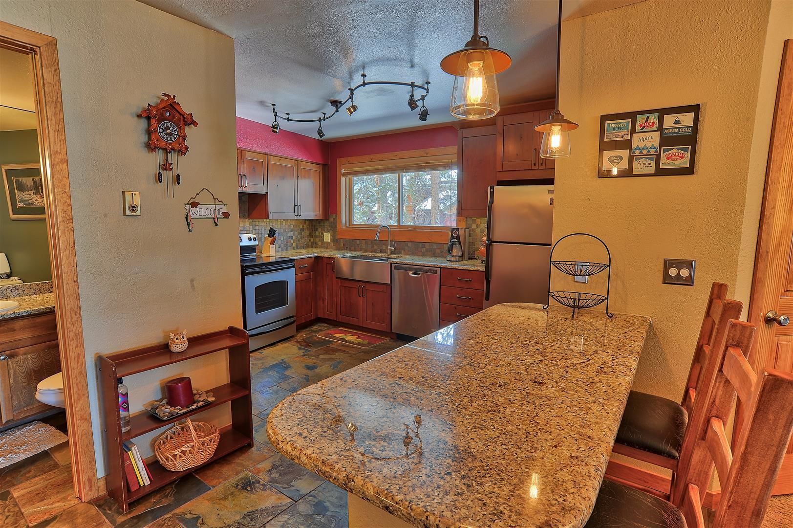 A kitchen with granite countertops, wooden cabinets, a built-in oven, a refrigerator, and a hanging light fixture.