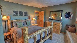 Un dormitorio con cabecera de cama de madera, cómoda, espejo y mesita de noche.
