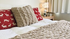 Un letto con una coperta beige e cuscini rossi con motivi di cervi, una lampada da comodino, una piccola pianta e una tazza da caffè su un comodino.