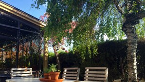 Una terrazza esterna con tavolo e panche in legno, immersa nel verde e alberi in fiore.