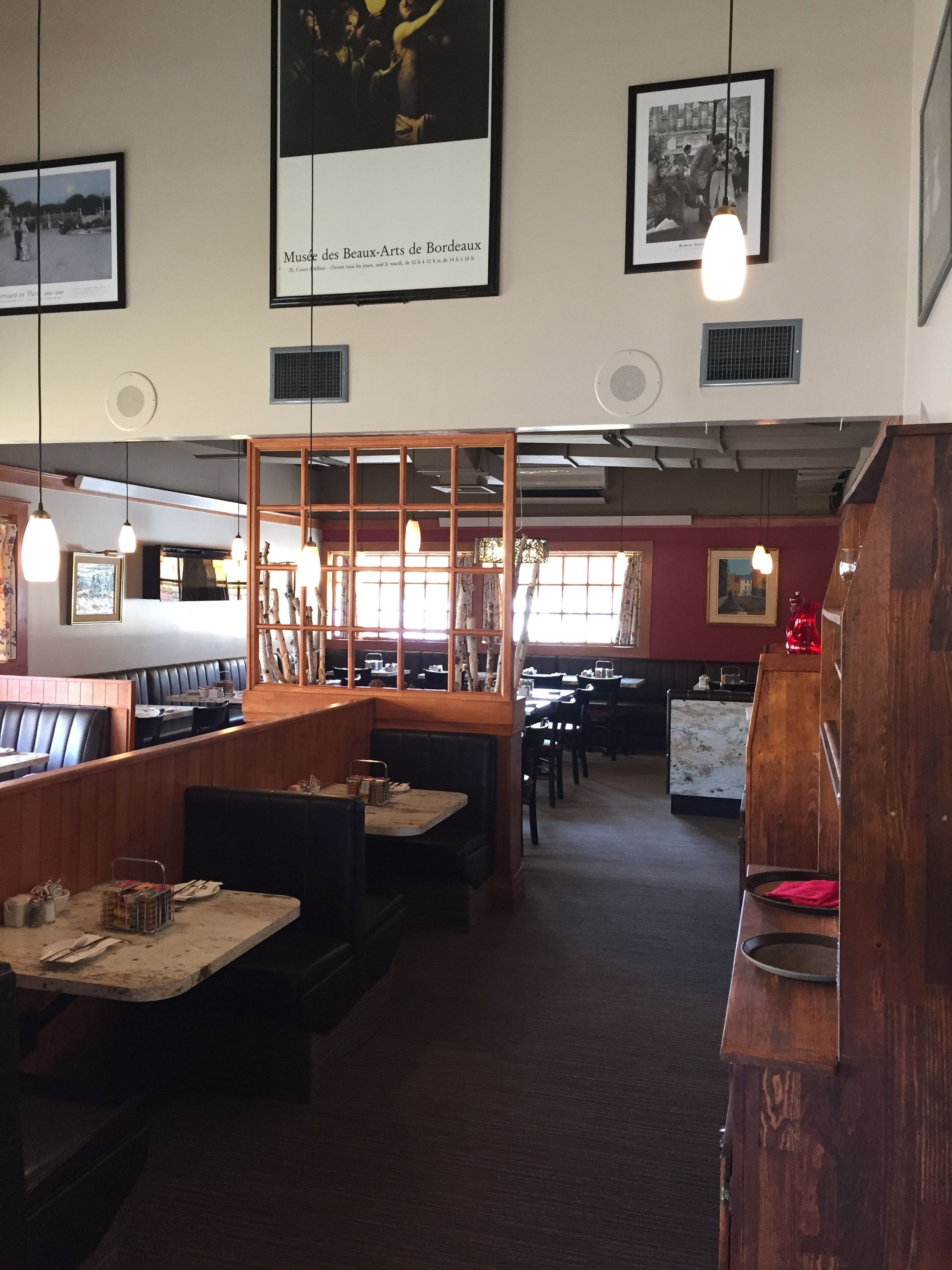 Interno di un ristorante con banquette, tavoli, lampade a sospensione e quadri appesi alle pareti.