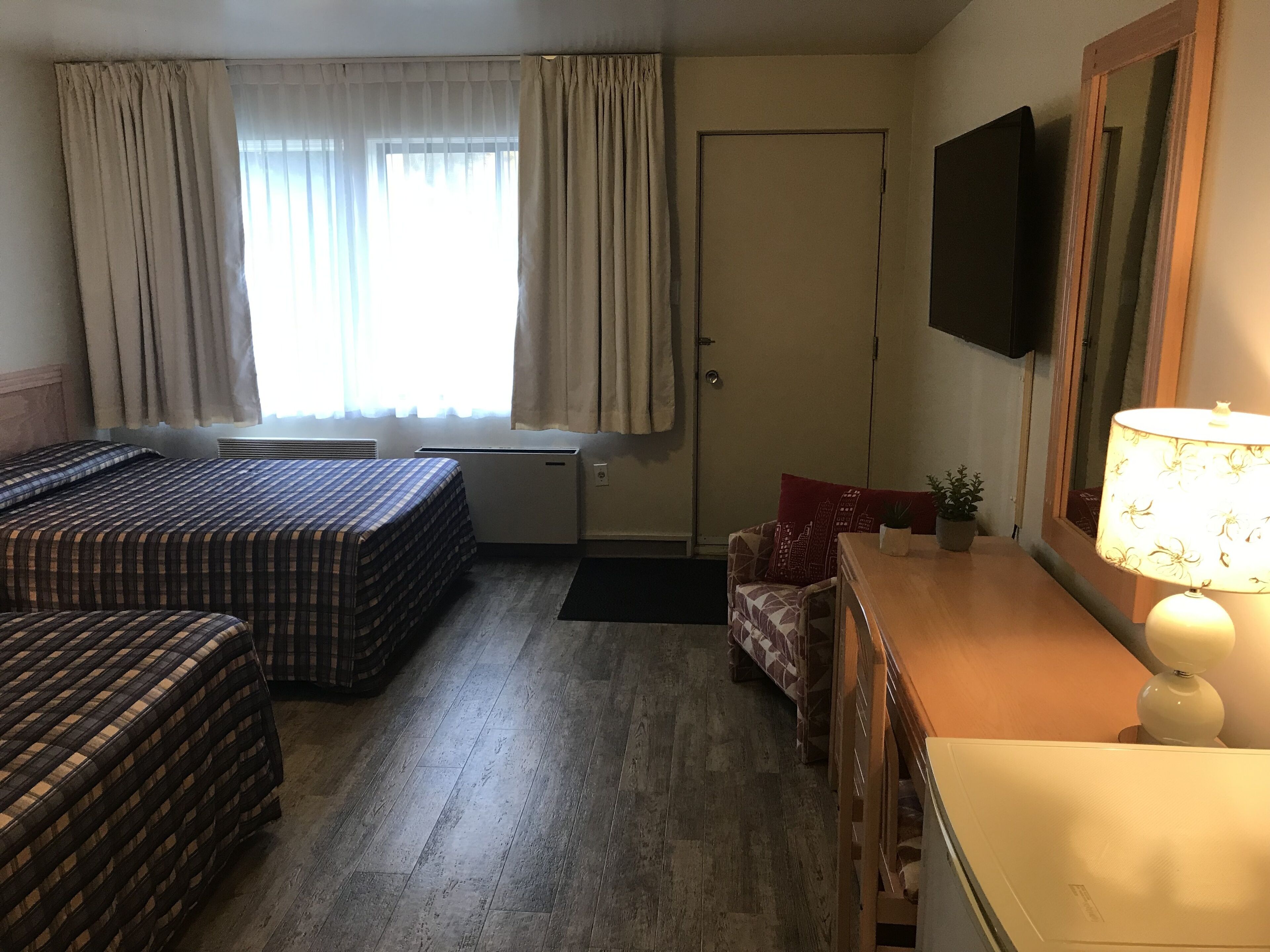 A hotel room with two beds, a desk, a chair, a TV, and a lamp.