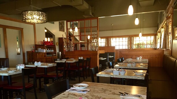 Un ristorante con tavoli e sedie in legno, un'area bar e vista all'esterno tramite ampie finestre.