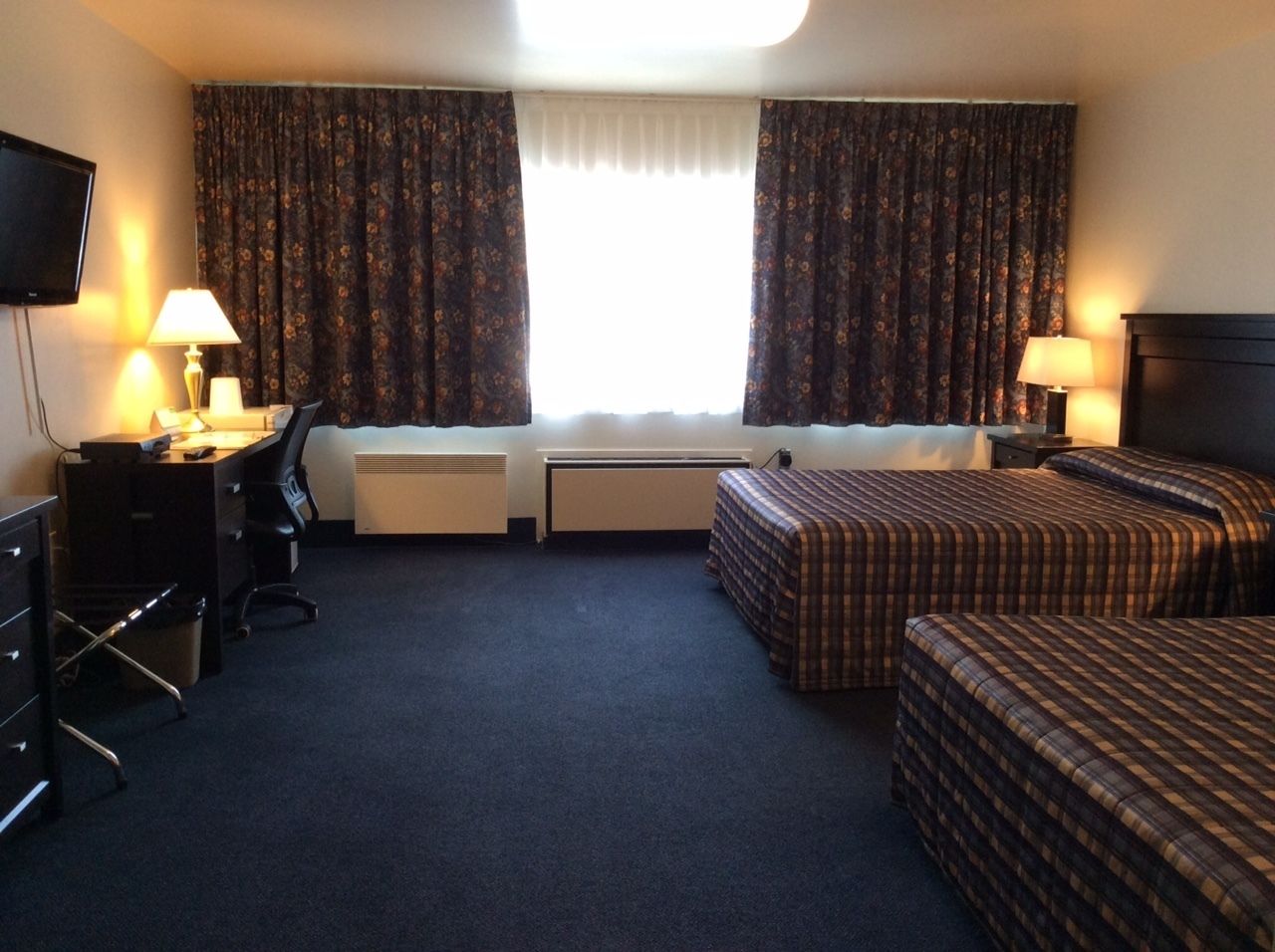 A hotel room with two beds, a desk, a chair, a TV, and a window with curtains.