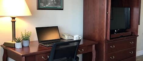 Et træskrivebord med en bærbar computer, en lampe og et billede i ramme på væggen.