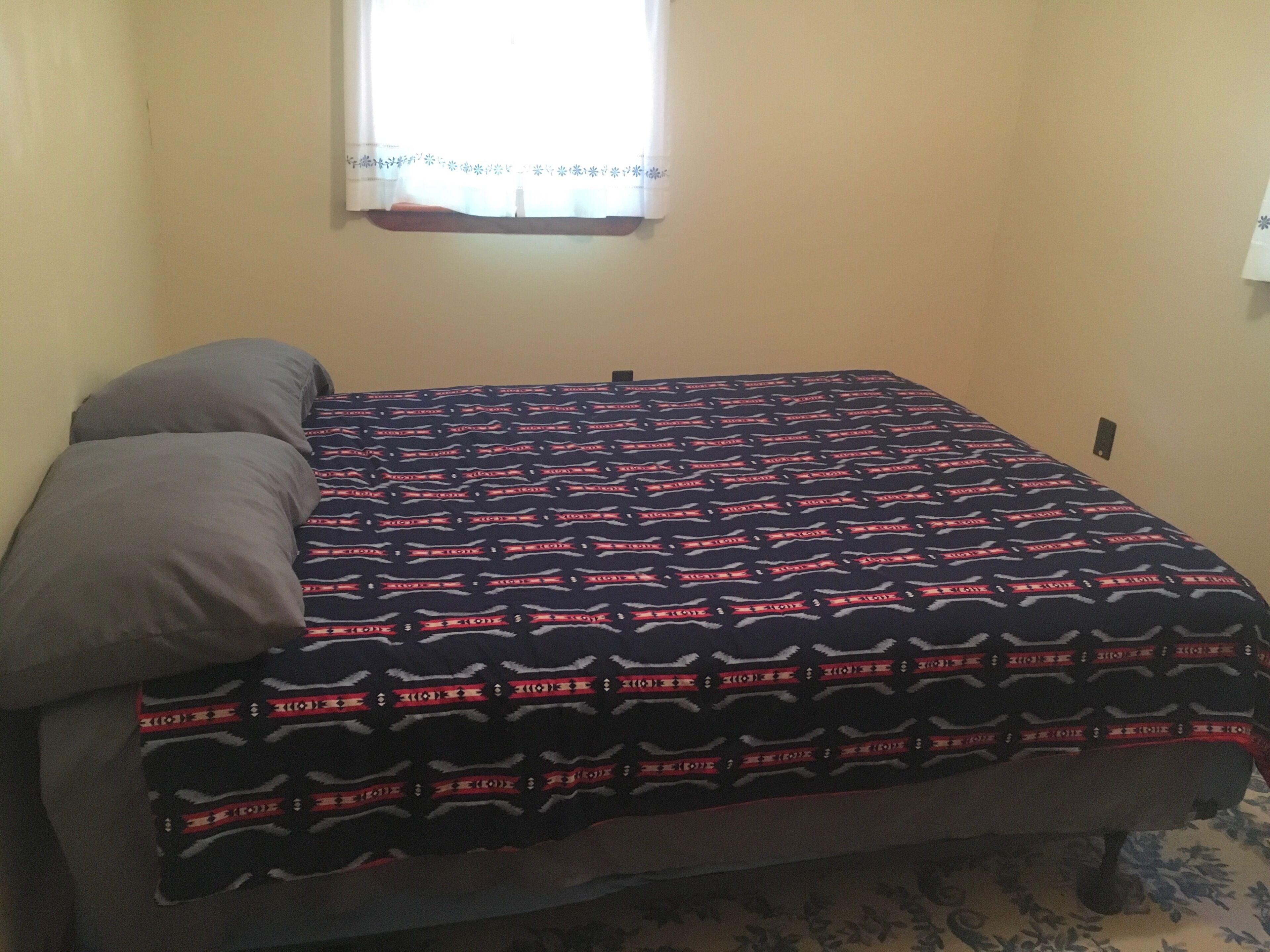 Una cama con una colcha estampada, una almohada y una ventana con cortina.