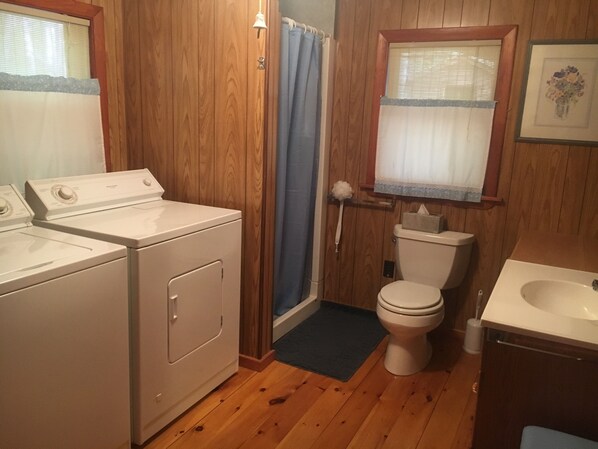 A compact bathroom with wooden walls, a toilet, a sink, and a washing machine.